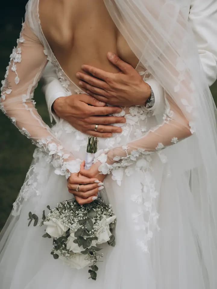 Nahaufnahme einer Umarmung mit Brautstrauß und Spitzenkleid